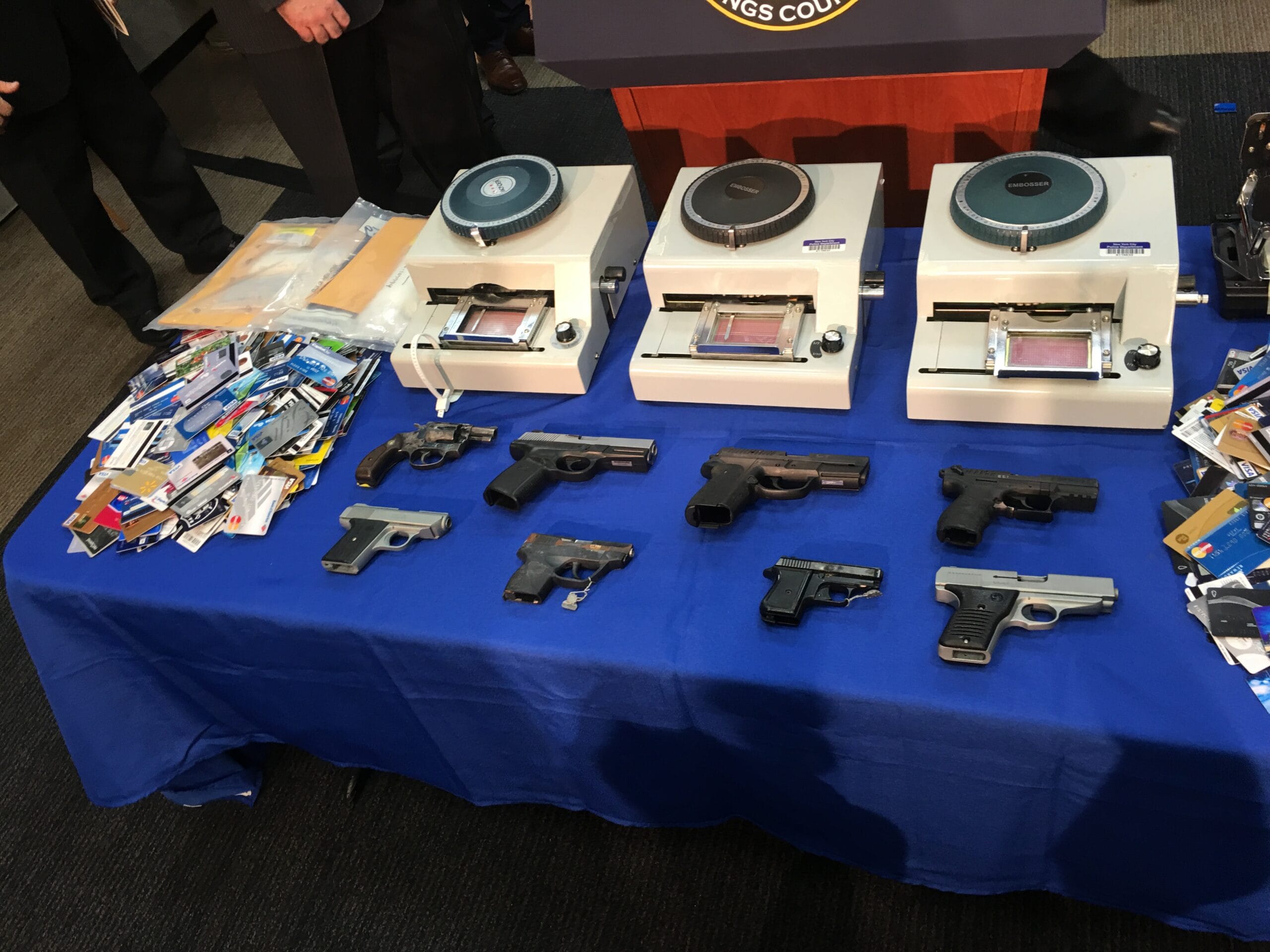 Assorted handguns and identification cards, displayed on a blue table during a press conference about crime prevention.