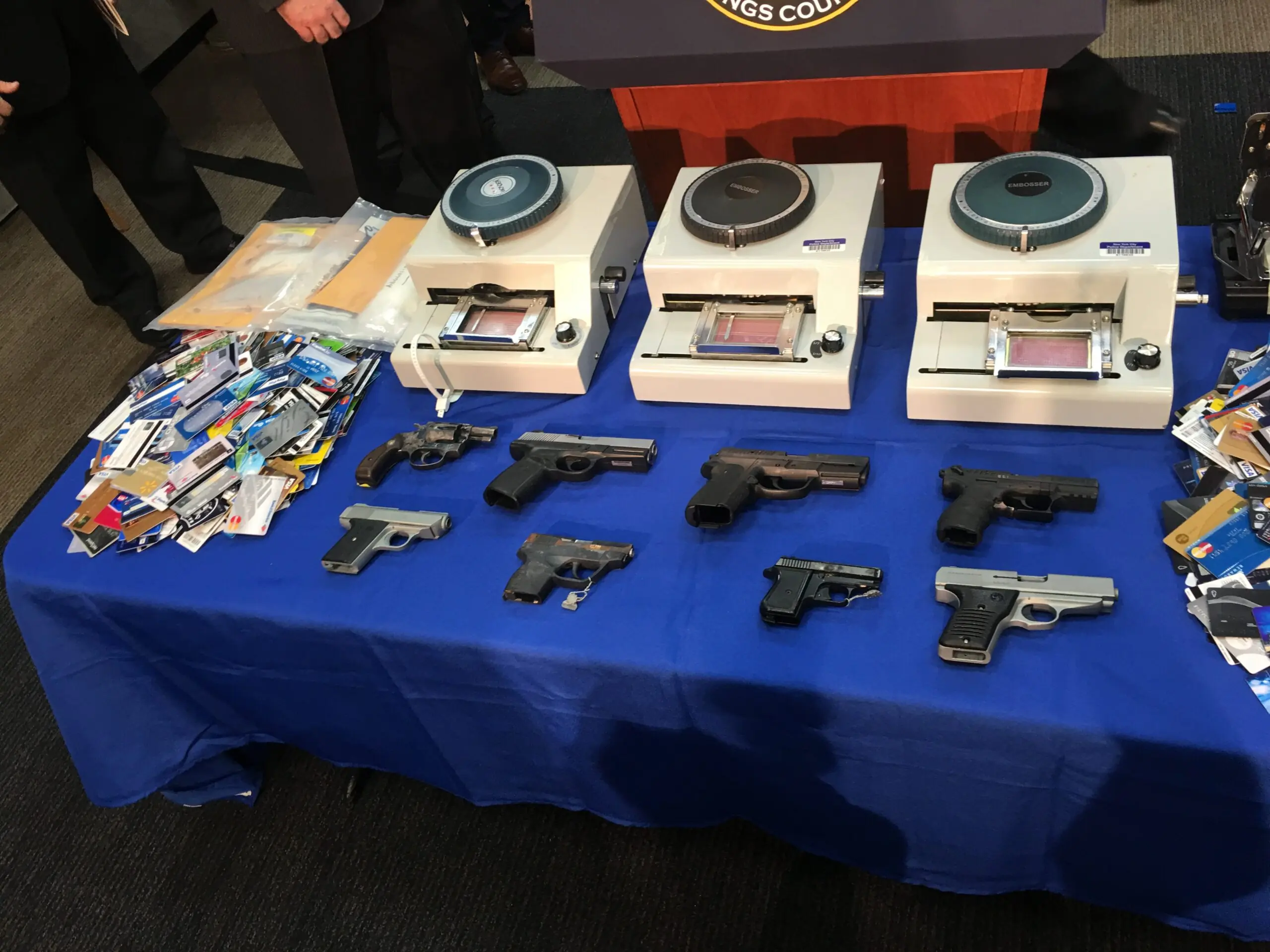 Assorted handguns and identification cards, displayed on a blue table during a press conference about crime prevention.